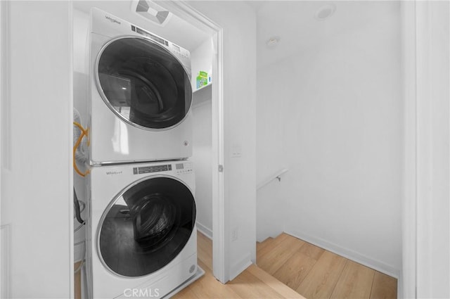 clothes washing area featuring baseboards, stacked washing maching and dryer, laundry area, and wood finished floors