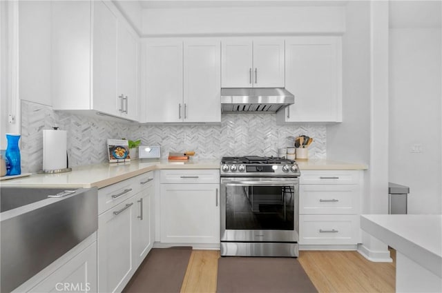 kitchen with light wood finished floors, white cabinetry, under cabinet range hood, light countertops, and gas stove