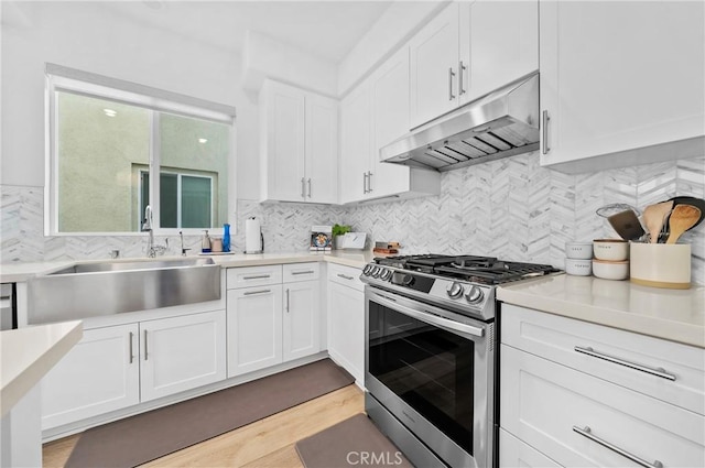 kitchen featuring stainless steel gas range, a sink, white cabinets, under cabinet range hood, and light countertops