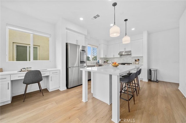 kitchen with a breakfast bar area, visible vents, under cabinet range hood, white cabinetry, and appliances with stainless steel finishes