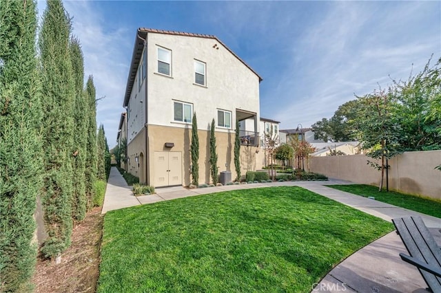 back of property with a yard, stucco siding, and fence