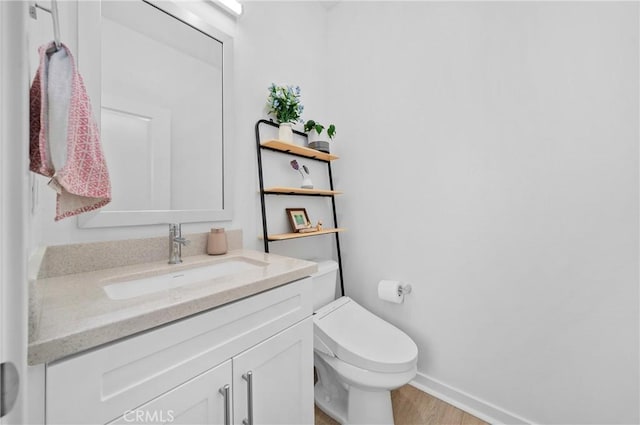 half bath with toilet, baseboards, vanity, and wood finished floors