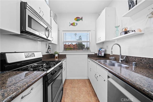 kitchen with light tile patterned flooring, white cabinets, stainless steel appliances, dark stone counters, and a sink