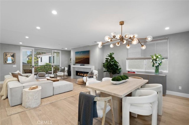 dining area with light wood-type flooring, a chandelier, a lit fireplace, and recessed lighting
