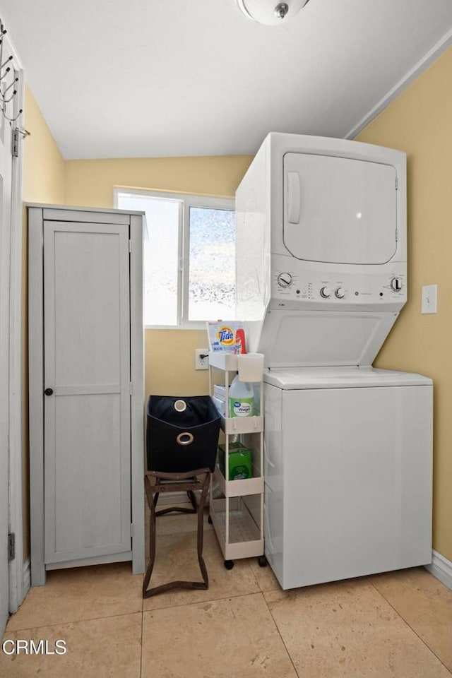 clothes washing area featuring stacked washer / dryer, laundry area, and light tile patterned floors