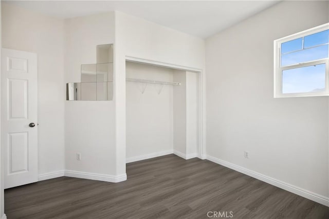 unfurnished bedroom with dark wood-style flooring, a closet, and baseboards