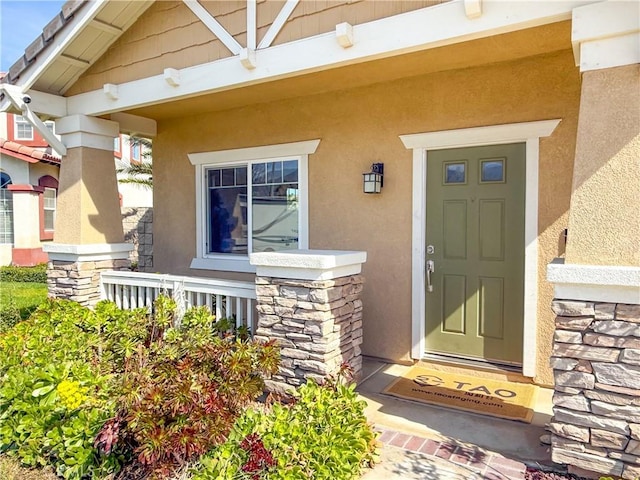view of exterior entry featuring stone siding, covered porch, and stucco siding