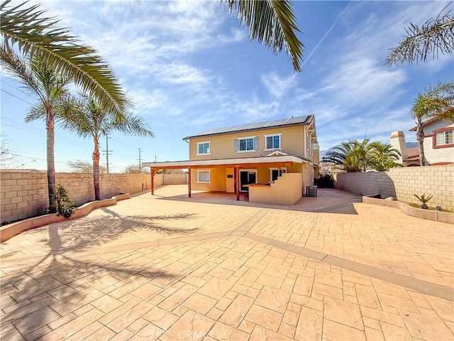 back of property with a fenced backyard, solar panels, stucco siding, and a patio