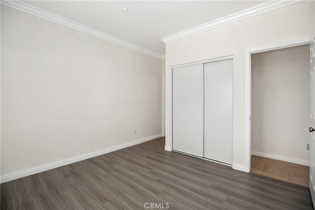 unfurnished bedroom with a closet, ornamental molding, baseboards, and wood finished floors