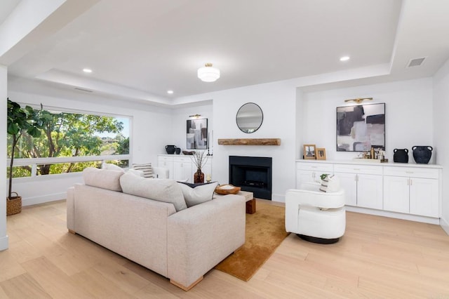 living area featuring a fireplace, a tray ceiling, and light wood-type flooring