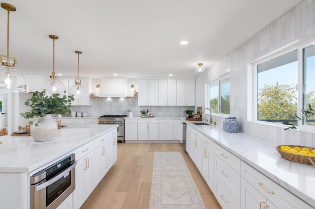 kitchen featuring decorative backsplash, appliances with stainless steel finishes, a sink, white cabinets, and light wood-style flooring