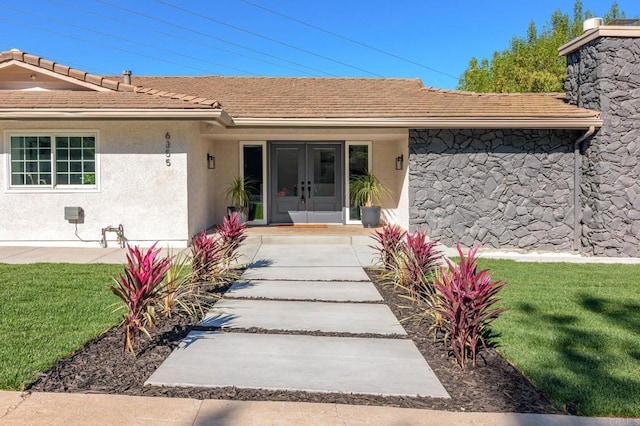 view of exterior entry with french doors, stucco siding, and a lawn