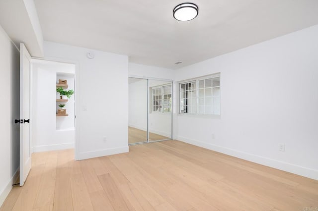 unfurnished bedroom featuring light wood-style floors, baseboards, and a closet
