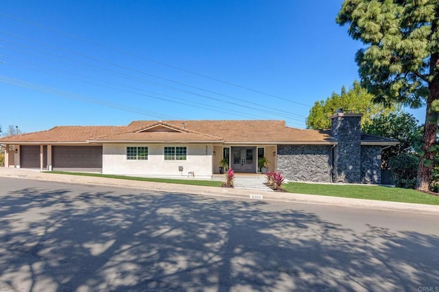 ranch-style house featuring an attached garage, stucco siding, a chimney, french doors, and driveway