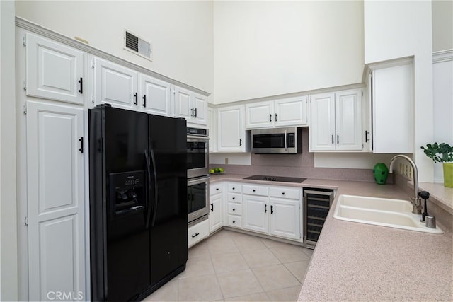 kitchen featuring a sink, visible vents, a towering ceiling, beverage cooler, and black appliances