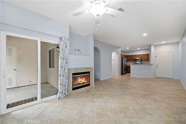 unfurnished living room featuring a ceiling fan, arched walkways, a tile fireplace, visible vents, and recessed lighting