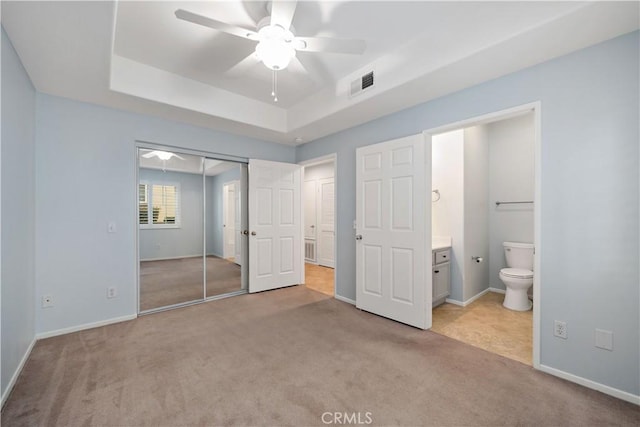 unfurnished bedroom with a tray ceiling, a closet, visible vents, and light carpet