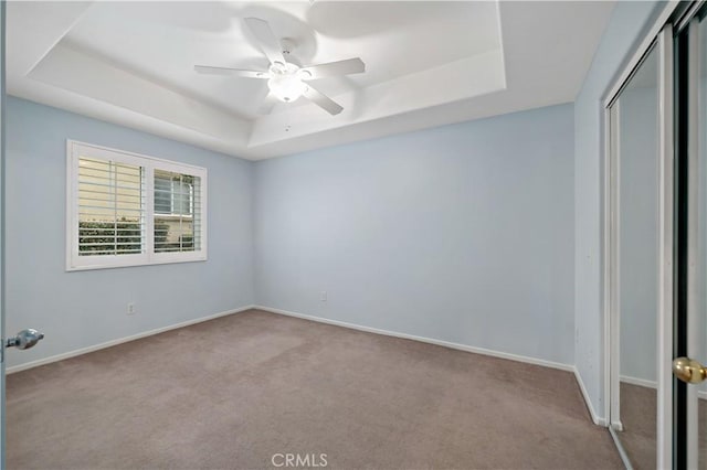 unfurnished bedroom with baseboards, carpet flooring, a tray ceiling, and a closet