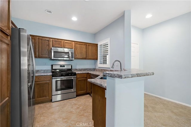 kitchen featuring stainless steel appliances, a peninsula, a sink, recessed lighting, and brown cabinetry