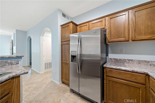 kitchen featuring visible vents, arched walkways, brown cabinets, and stainless steel fridge with ice dispenser