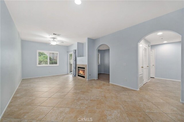 unfurnished living room with a ceiling fan, a glass covered fireplace, visible vents, and light tile patterned floors