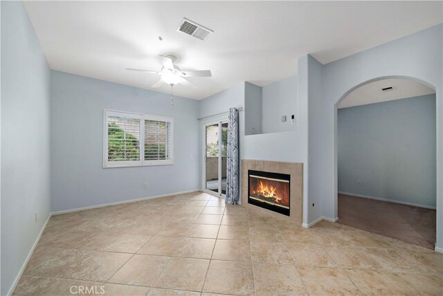 unfurnished living room featuring visible vents, a ceiling fan, arched walkways, baseboards, and a tiled fireplace