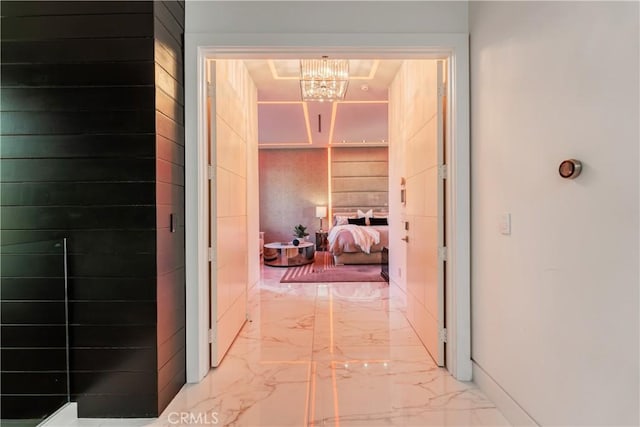 corridor with marble finish floor and an inviting chandelier