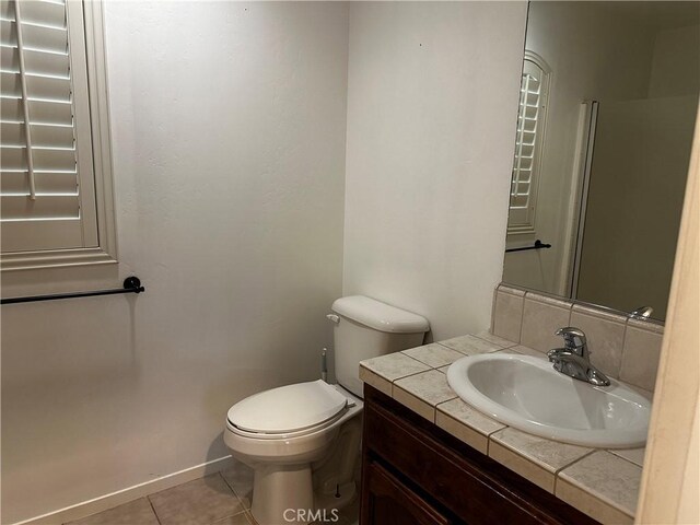 half bath featuring toilet, vanity, tile patterned floors, and baseboards
