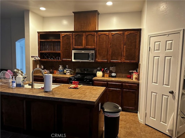 kitchen featuring tasteful backsplash, dark brown cabinetry, gas range oven, and stainless steel microwave