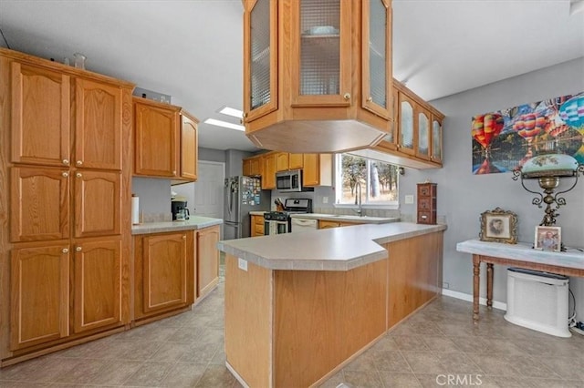 kitchen featuring light countertops, stainless steel appliances, a sink, a peninsula, and glass insert cabinets
