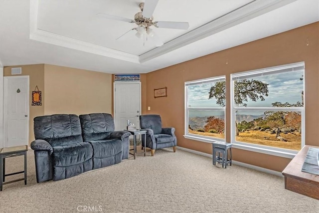 carpeted living room with visible vents, baseboards, ceiling fan, ornamental molding, and a tray ceiling