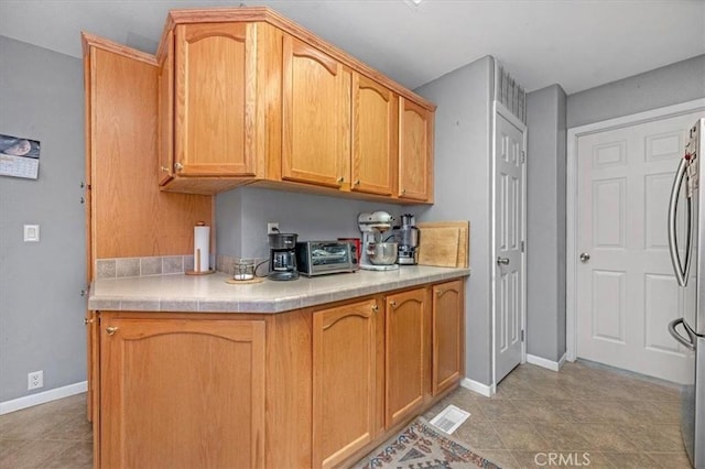 kitchen featuring baseboards, visible vents, stainless steel fridge, and a toaster