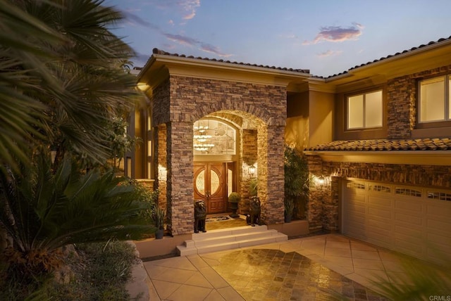 5023 Windsor Dr, San Diego, CA 92109 - exterior entry at dusk featuring stone siding, stucco siding, a garage, and a tiled roof