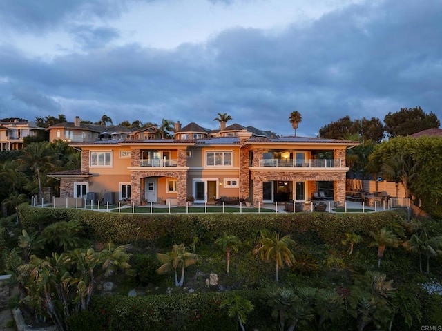 5023 Windsor Dr, San Diego, CA 92109 - rear view of house with a balcony, a fenced backyard, roof mounted solar panels, and stone siding