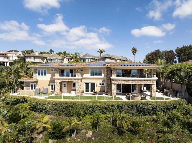 5023 Windsor Dr, San Diego, CA 92109 - rear view of property with a balcony, stone siding, a fenced backyard, and roof mounted solar panels