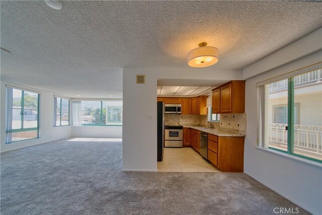 201 Calle Miramar Unit 16, Redondo Beach, CA 90277 - kitchen featuring stainless steel appliances, brown cabinetry, open floor plan, light carpet, and a textured ceiling