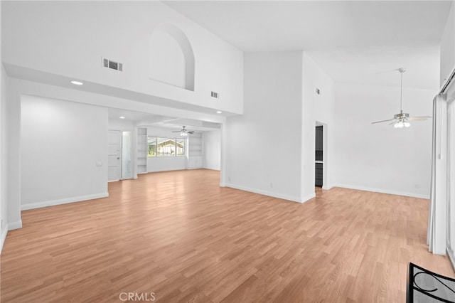 unfurnished living room with visible vents, baseboards, a ceiling fan, and a towering ceiling