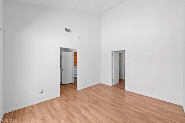 empty room with high vaulted ceiling, baseboards, light wood-style floors, and visible vents
