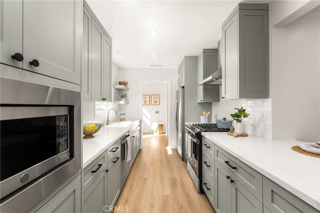 kitchen with appliances with stainless steel finishes, open shelves, light wood-type flooring, light stone counters, and ventilation hood