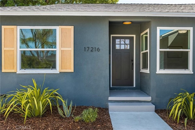 doorway to property with stucco siding and a shingled roof