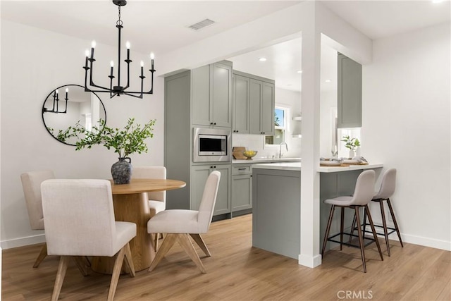 kitchen featuring gray cabinetry, a kitchen bar, light wood-style flooring, and stainless steel microwave