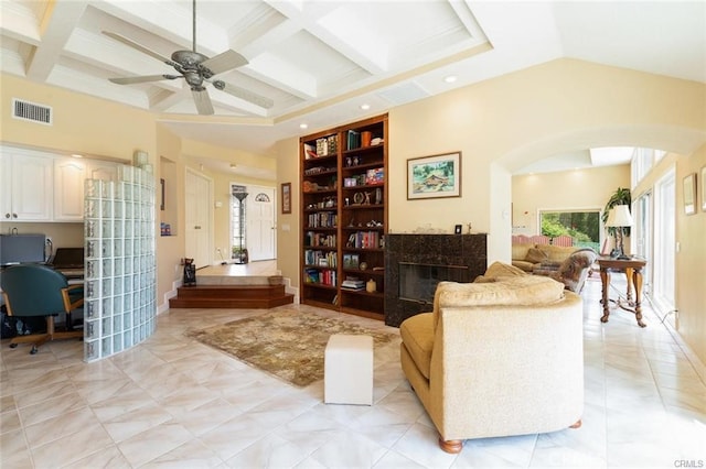 living area featuring coffered ceiling, a premium fireplace, arched walkways, ceiling fan, and visible vents