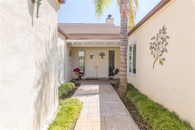 view of exterior entry with stucco siding and a chimney