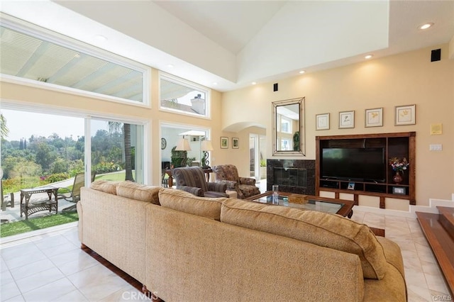 living room with high vaulted ceiling, arched walkways, a glass covered fireplace, and light tile patterned floors