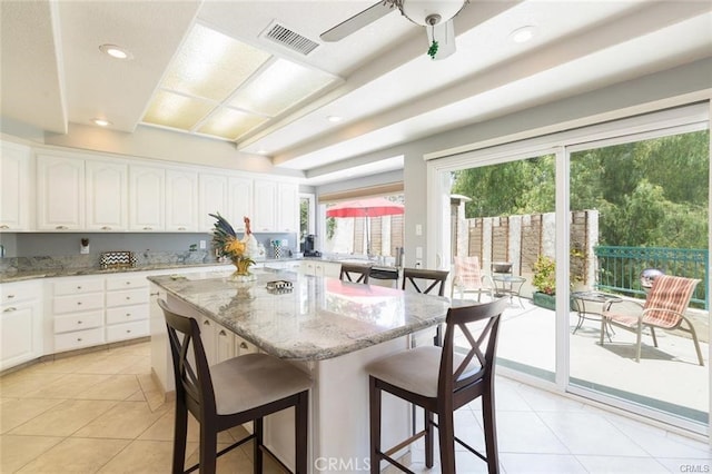 kitchen featuring white cabinets, a breakfast bar area, light stone counters, and visible vents
