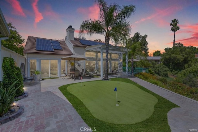 rear view of house with a chimney, stucco siding, solar panels, a tiled roof, and a patio
