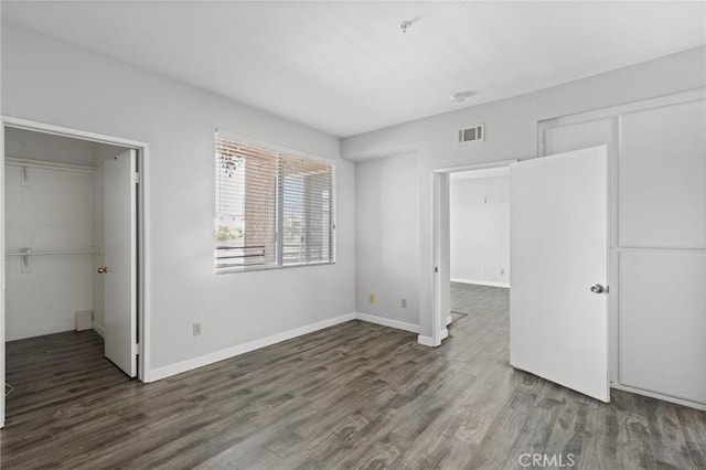 unfurnished bedroom featuring a spacious closet, visible vents, a closet, and wood finished floors