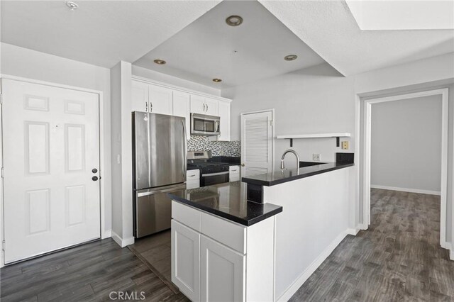 kitchen with a peninsula, white cabinets, appliances with stainless steel finishes, dark wood-style flooring, and dark countertops