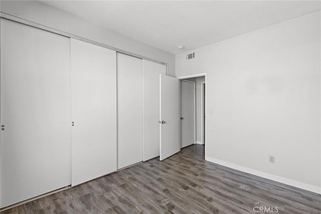 unfurnished bedroom with a closet, wood finished floors, baseboards, and visible vents