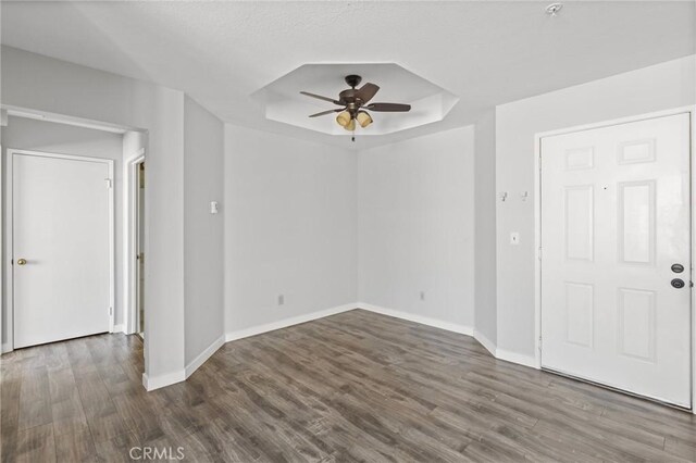 spare room with a tray ceiling, wood finished floors, ceiling fan, and baseboards